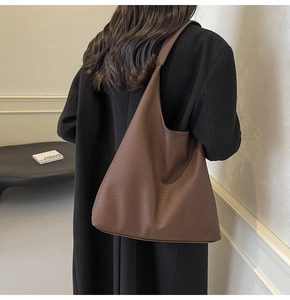 Deep brown pebble leather tote bag shown on a model in a minimalist indoor setting