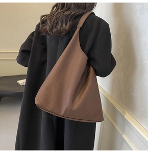 Close-up of a large brown leather hobo bag worn by a model in a black winter coat