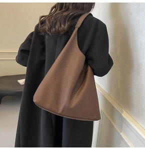 Detail of a large dark brown tote bag with triangular cut design worn by a model