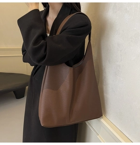 Detail view of large brown textured leather tote bag worn as an underarm shoulder bag