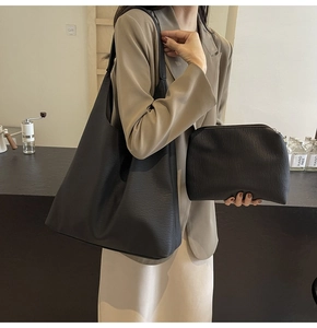 Detail view of large black leather tote bag with matching zippered pouch and pebbled texture