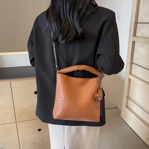 Sac seau marron à texture tressée avec chaîne en métal et pompon porté par un mannequin
