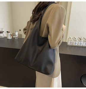 Lifestyle view of a large black leather tote bag with wide strap in a cafe setting