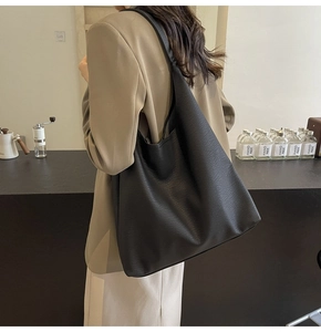 Lifestyle view of a large black faux leather tote bag worn by a model in a cafe