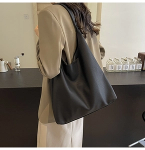Detail of a large black leather tote bag with lychee texture worn with a beige blazer