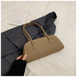 Detail of light brown leather baguette bag with white stitching on a grey blazer