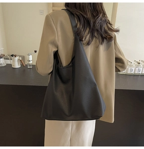 Close-up of black lychee grain PU leather tote bag worn over the shoulder by a model