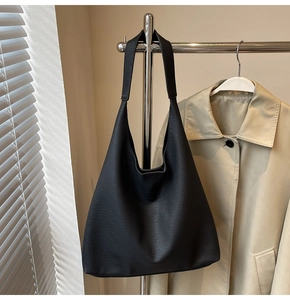 Detail of black large tote bag with lychee texture hanging on a minimalist stand