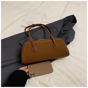 Close-up of brown matte tote bag with white stitching details and top zipper on grey suit
