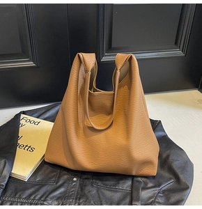 Close-up of brown litchi pattern leather tote bag on black jacket and books background