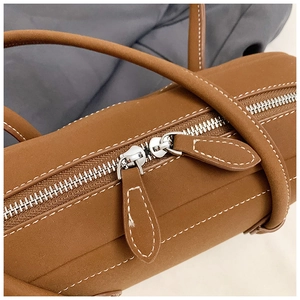 Detail shot of brown leather tote bag showing white contrast stitching and silver zipper