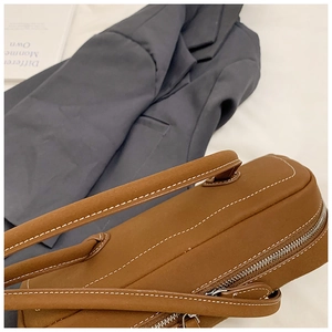 Detail view of brown tote bag with white contrast stitching and premium metal zipper
