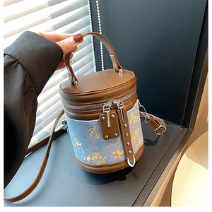 Détail du sac seau en denim bleu avec broderie fleurie dorée et poignée en cuir brun