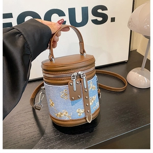 Détail du sac seau cylindrique avec broderie florale et finitions en cuir marron
