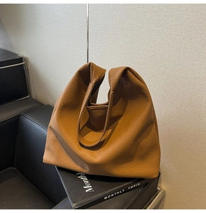 Macro shot of brown leather tote bag with lychee texture resting on a black book