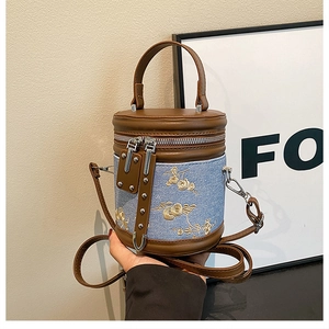 Détail du sac seau en denim bleu avec broderie florale et garniture en cuir marron