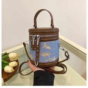 Détail du sac seau en denim bleu avec broderie florale et anses en cuir marron élégant