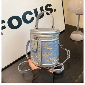 Détail du sac seau en denim bleu clair avec broderies de fleurs dorées et finitions argent