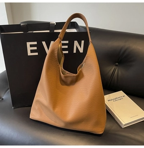 Detail of large brown pebble leather tote bag with wide shoulder strap on sofa
