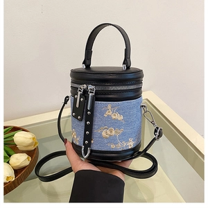 Détail d'un sac seau en cuir noir avec denim bleu et motif de broderie florale