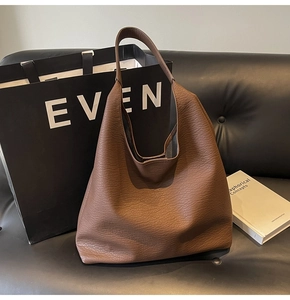 Deep brown large capacity tote bag made of lychee grain leather displayed on leather sofa