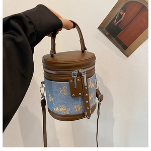 Détail du sac seau en denim avec broderie florale dorée et finitions en cuir marron
