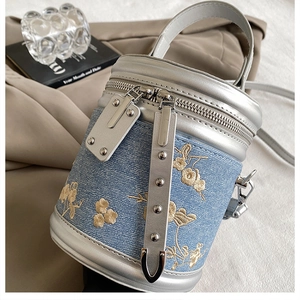 Détail de broderie florale et fermetures éclair argentées sur un sac baril en denim