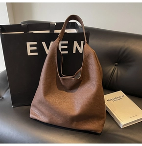 Close-up of a large dark brown lychee texture leather hobo bag on a leather sofa