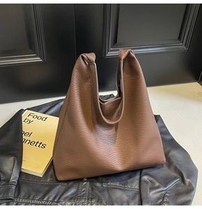 Close-up of brown pebbled leather tote bag placed on a black jacket with a book