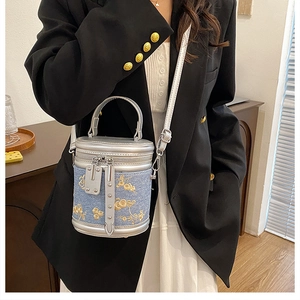 Détail du sac cylindrique en denim bleu avec broderies dorées et finitions en cuir argenté