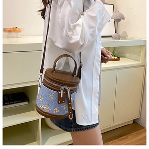Détail du sac seau en denim bleu avec broderie florale dorée et garniture en cuir marron