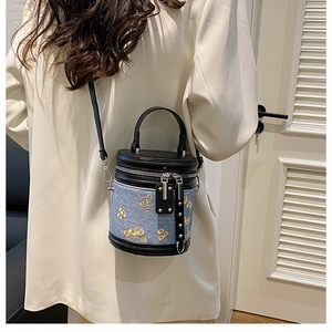 Détail de broderie florale sur sac seau en denim bleu avec finitions en cuir noir