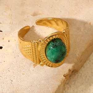 Detail of wide gold stainless steel ring with green natural stone on textured rock