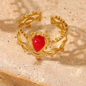 Macro detail of gold crown ring featuring a red teardrop stone on beige marble