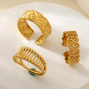Three gold stainless steel open rings with geometric and filigree designs on stone base