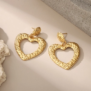 Golden heart-shaped drop earrings with hammered texture on a minimalist stone background