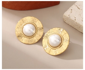 Close-up of golden hammered metal earrings featuring central pearl and vintage beaded edge
