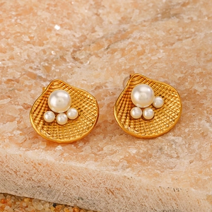 Close-up of 18k gold plated shell earrings with large pearl accents on natural stone