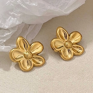 Orecchini a perno a forma di fiore dorato a cinque petali su uno sfondo beige testurizzato