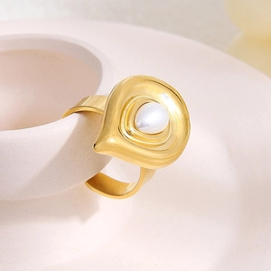 Detail of an irregular gold-plated ring with a pearl on a cream ceramic surface