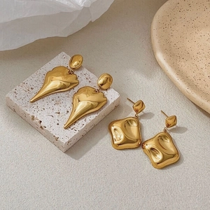 Macro detail of irregular gold leaf and square earrings on a stone base display