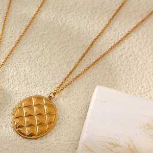 Collier doré avec pendentif rond à motif matelassé sur marbre blanc et décor herbe