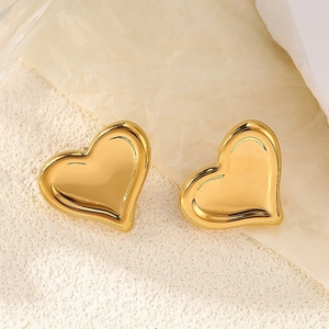 Détail des boucles d'oreilles cœur dorées polies sur un fond minimaliste texturé