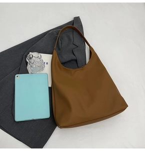 Detailed view of brown leather tote bag with gray blazer and tablet on white fabric