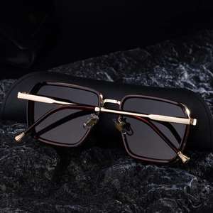 Close-up of square sunglasses featuring premium gold metal temples on dark stone background