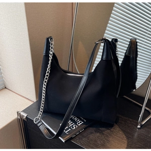 Détail du sac hobo noir avec chaîne argentée et bandoulière en cuir sur bois