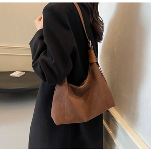 Sac hobo en daim marron avec logo embossé porté avec un manteau en laine noire