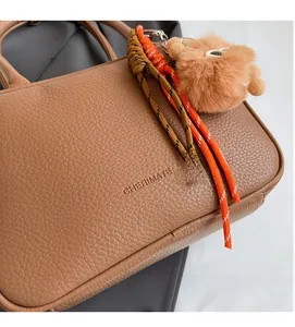 Nahaufnahme der braunen Handtasche mit Lederstruktur, Plüschball und Seilanhänger