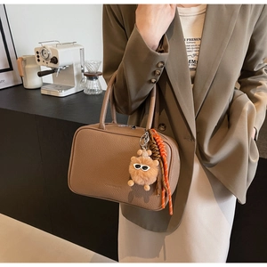 Detailed shot of brown litchi grain leather handbag with cute bear charm and woven keychain