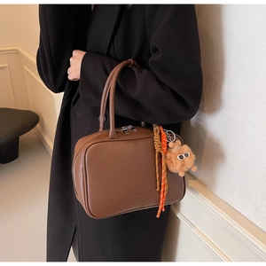 Detail of brown litchi pattern leather bowling bag with plush doll and woven pendant
